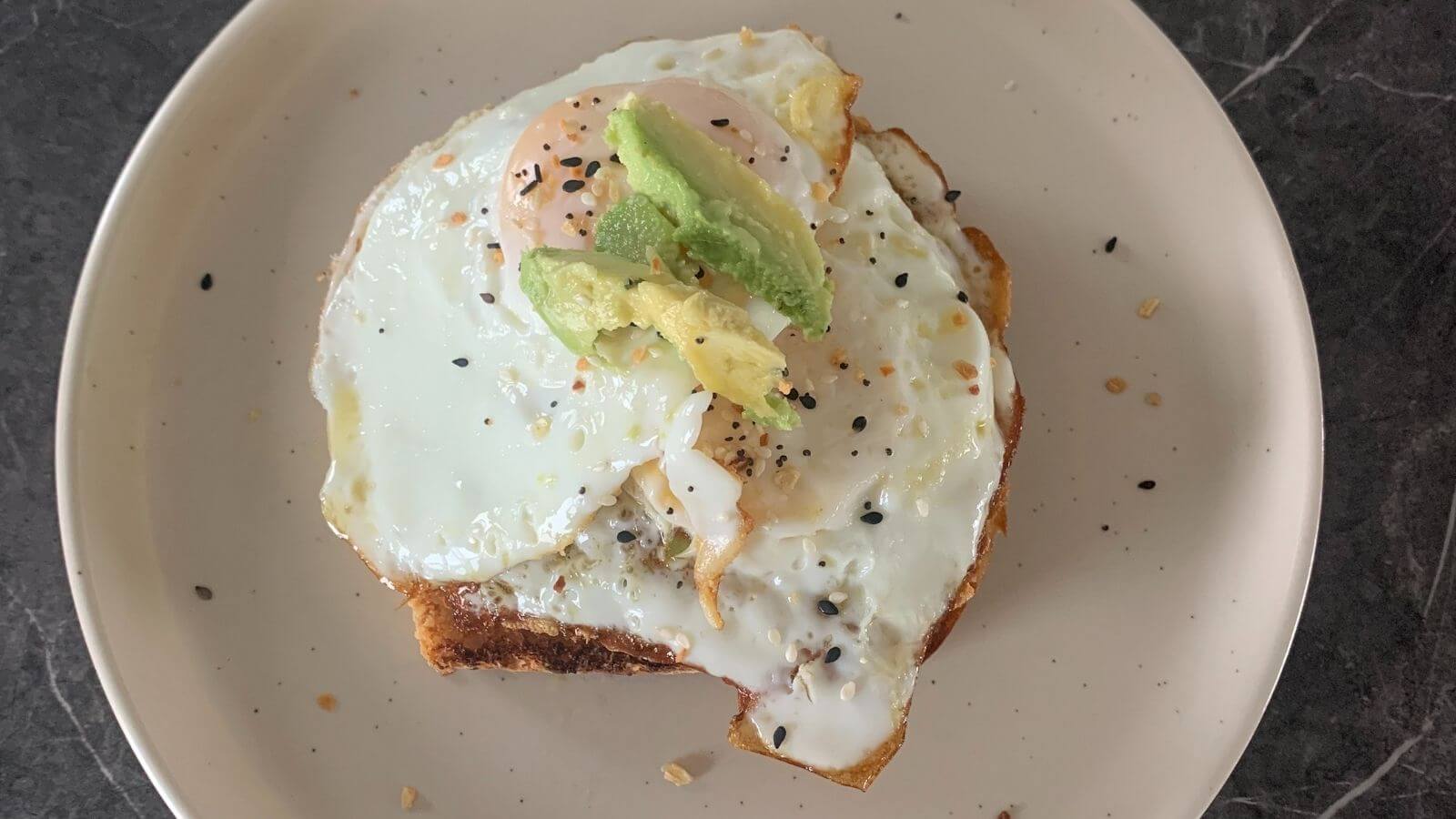 plated fried egg topped with sliced avocado on top of toast
