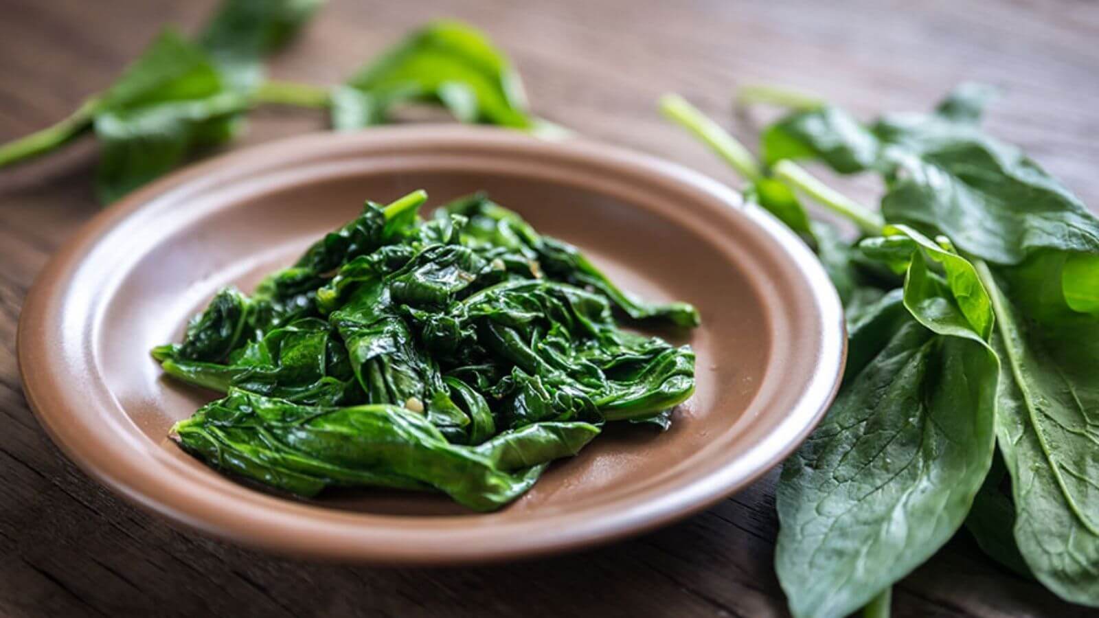 sautéed spinach on a plate surrounded by spinach leaves