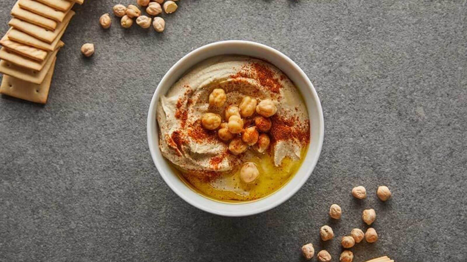 bowl of hummus topped with chickpeas, surrounded by chickpeas and crackers