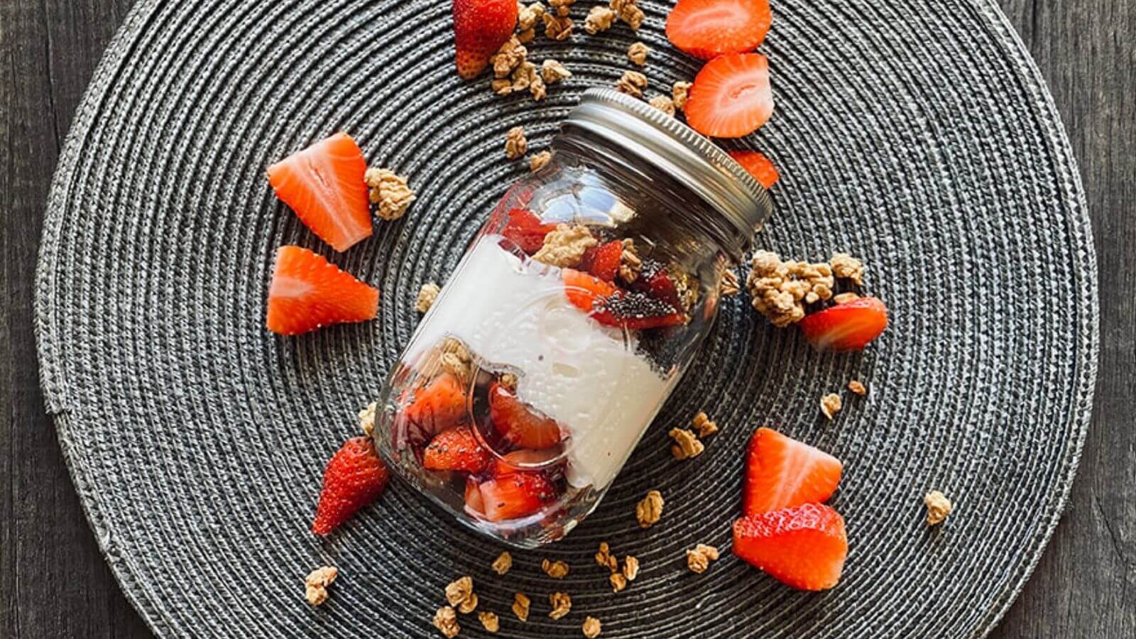 mason jar filled with Greek yogurt, strawberries, chia seeds, and granola, surrounded by sliced strawberries and granola