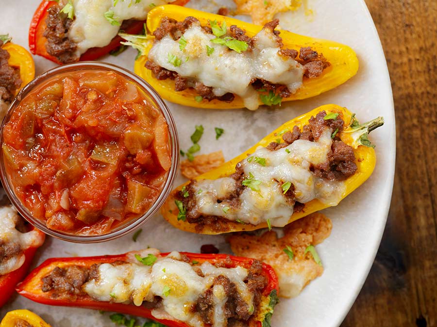 halved yellow and red bell peppers filled with taco meat and cheese, served with a dish of salsa 