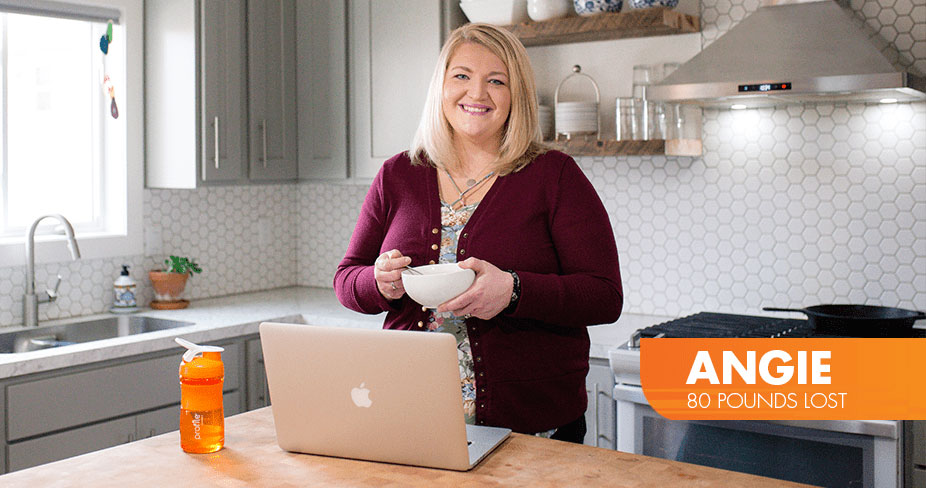 Angie Lost 80 pounds with Profile by Sanford. Photo of Angie with a bowl standing with her laptop in her kitchen.