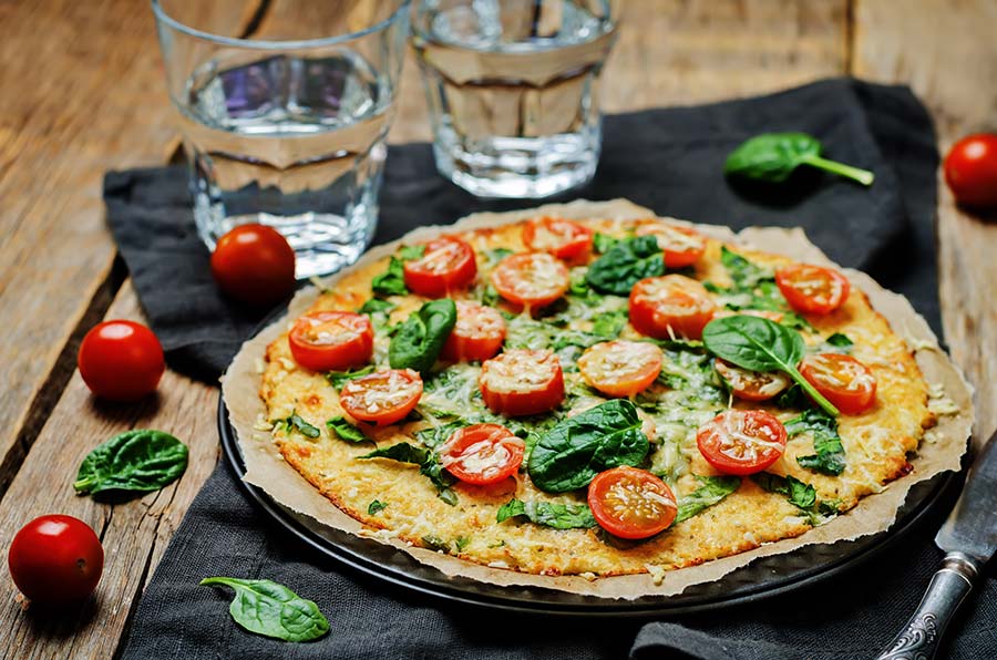 thin crust pizza topped with spinach and tomatoes