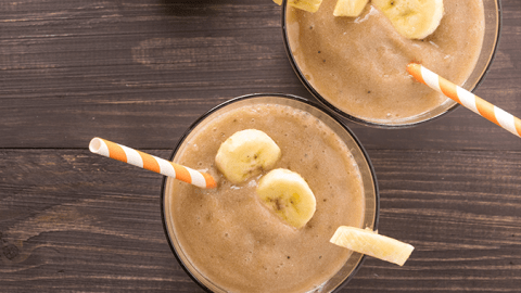 chocolate shake in a glass topped with sliced bananas and a straw
